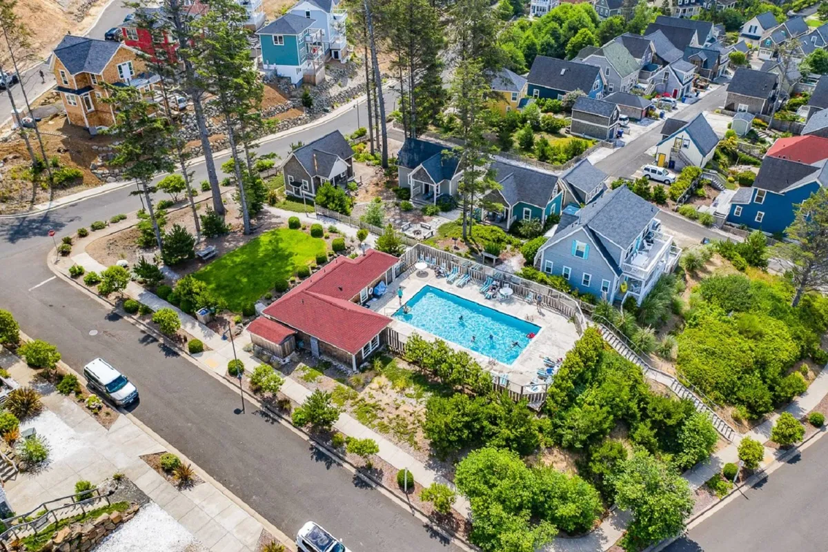 A vibrant exterior shot of the community’s heated saltwater swimming pool, surrounded by green landscaping and adjacent to a red-roofed building. The pool area is sunlit and welcoming, ideal for family swim sessions, playful afternoons, or relaxing while children have fun in the water.