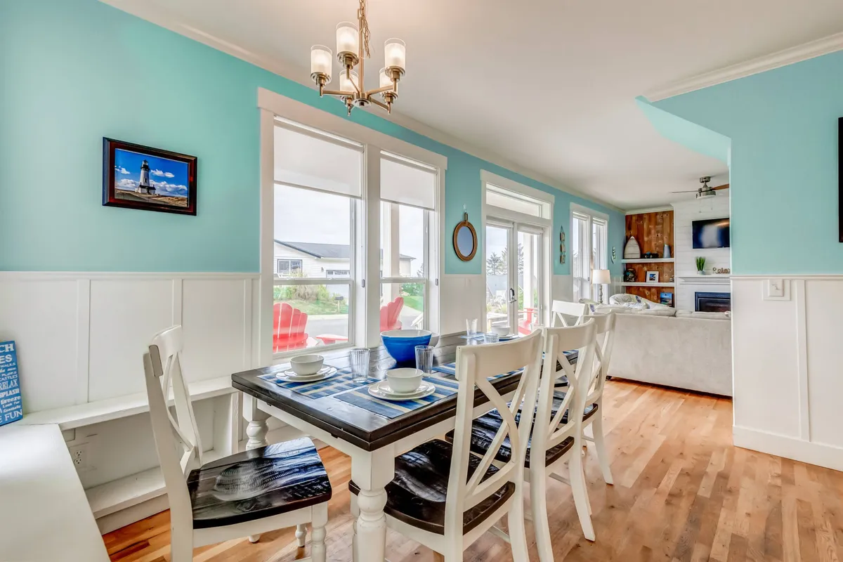 A dining table with elegant place settings next to large windows, flooding the space with natural light. Decorative wall art and a comfortable seating area in the background set a cheerful, inviting tone for group dining.