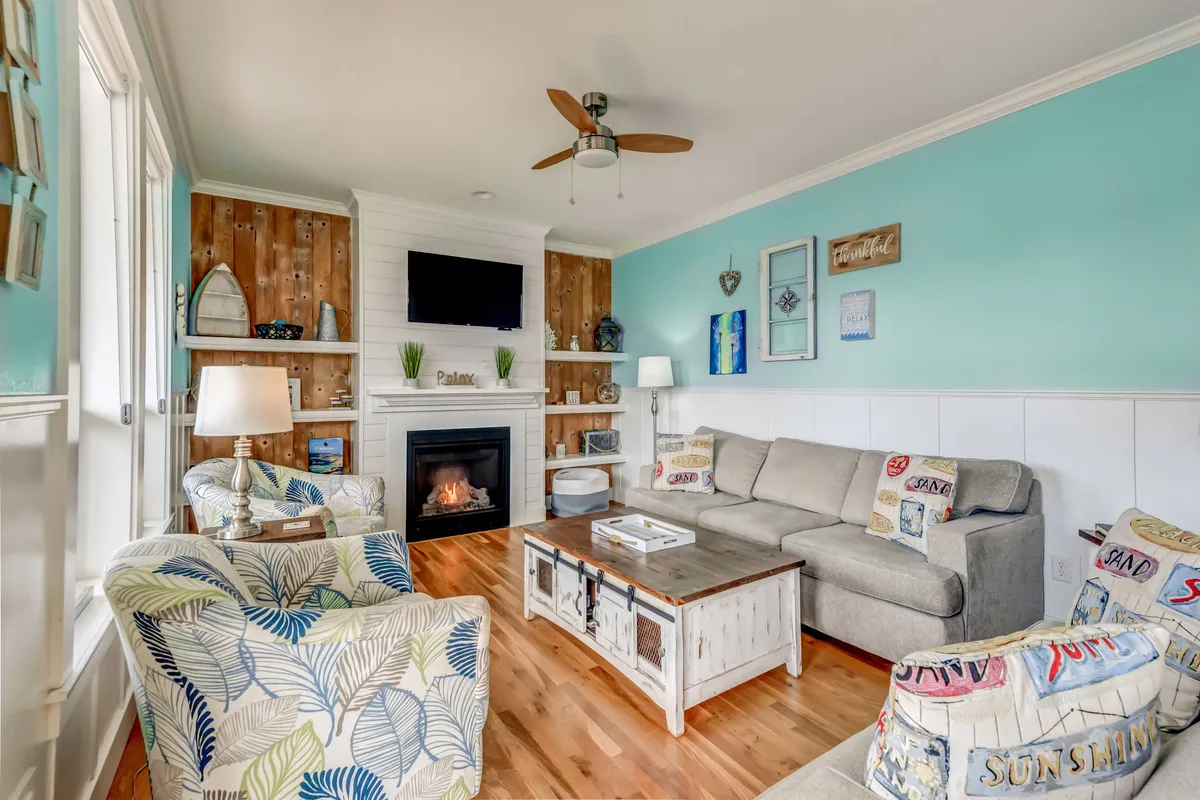 A warm, inviting living room featuring a plush sofa, a stylish coffee table, and a gas fireplace as the central focal point. Decorative wall art adds personality while daylight streams in from adjacent windows, enhancing the cozy ambiance.