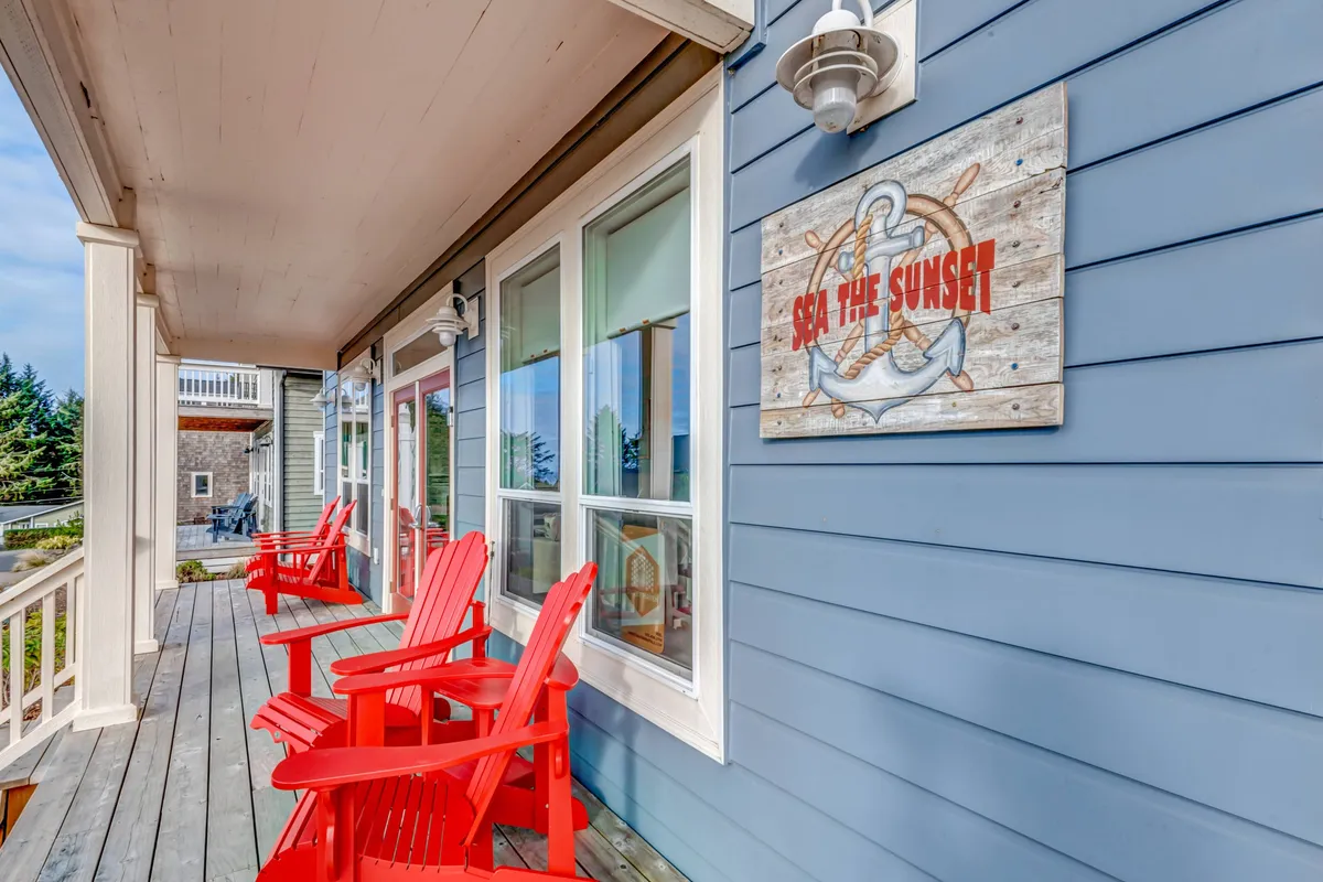 A cozy and cheerful exterior view featuring red Adirondack chairs on a wooden deck, the 'Sea the Sunset' sign, and a welcoming porch. The scene captures the spirit of togetherness, relaxation, and enjoying sunsets after a day of adventure.
