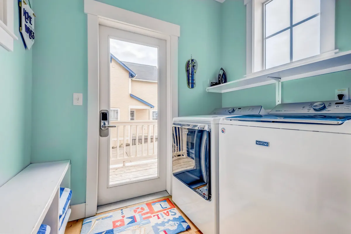 A practical laundry area with a washing machine, dryer, and a door leading directly to the outside. The presence of bright natural light and a colorful rug adds a cheerful tone, and the exterior-facing door hints at easy transitions between indoor comforts and outdoor adventures.