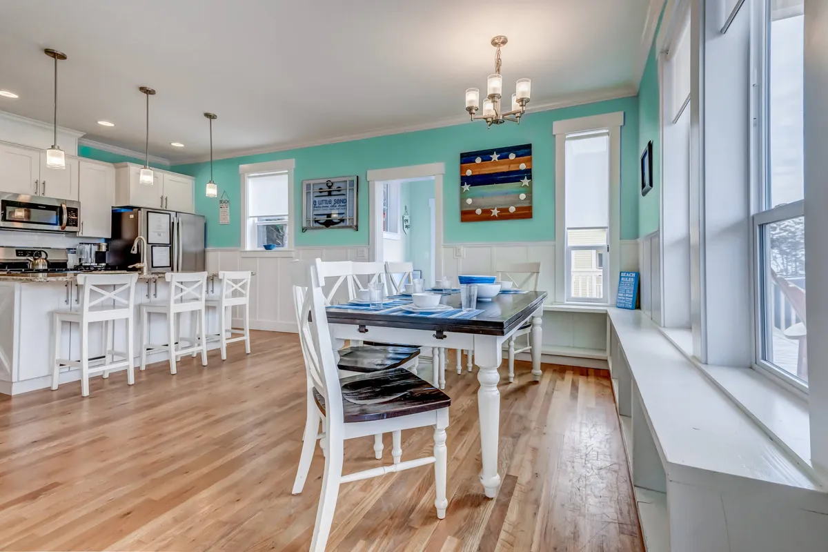 An expansive kitchen and dining area with a large table set for a family meal, a bright kitchen island, vibrant blue walls, and colorful artwork. The image exudes warmth, togetherness, and space to gather, cook, and share meals.