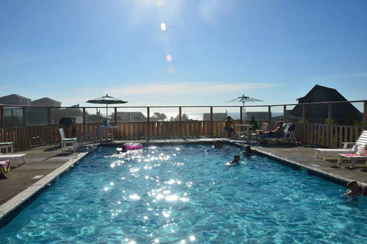 A lively community pool scene featuring sun loungers, umbrellas, and people enjoying the water. The atmosphere is joyful and vibrant, highlighting the pool as a hub of activity and leisure within the community.