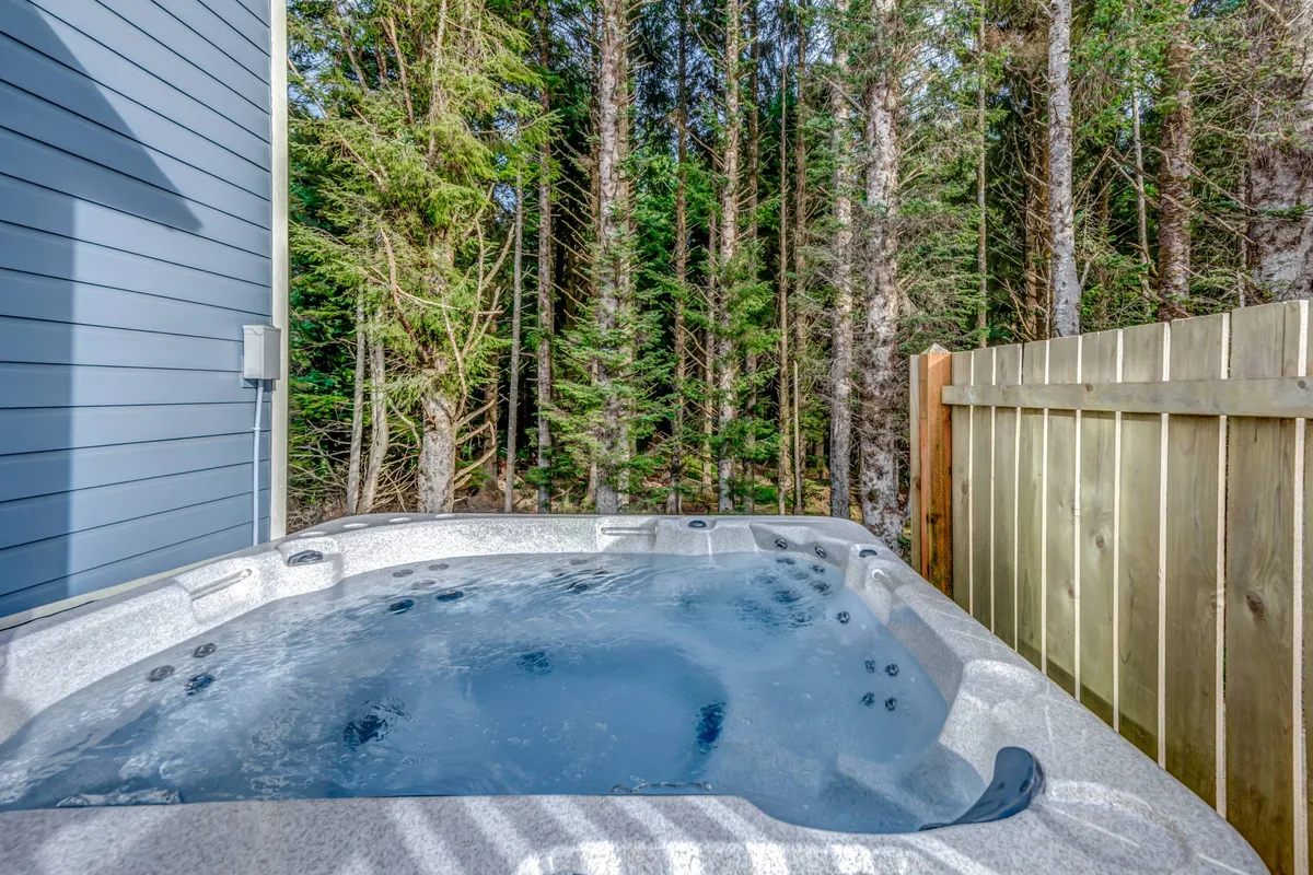 This image showcases a serene private hot tub surrounded by trees and a privacy fence. The scene is tranquil, with open sky above and a sense of immersion in nature. The area is perfect for relaxation, stargazing, and soaking up the outdoors in a private setting.